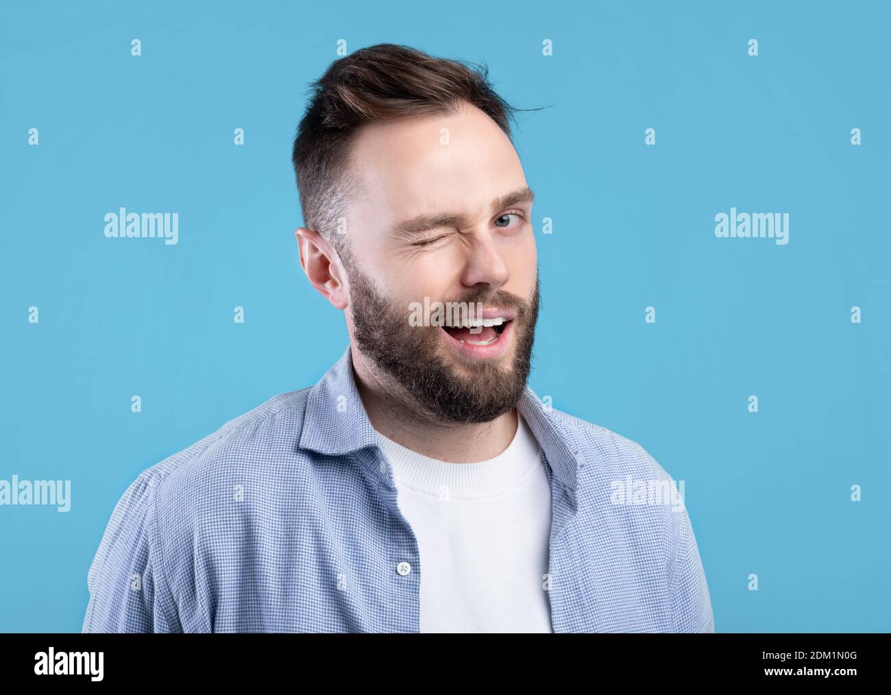 Confident handsome Caucasian man winking and smiling at camera on blue ...