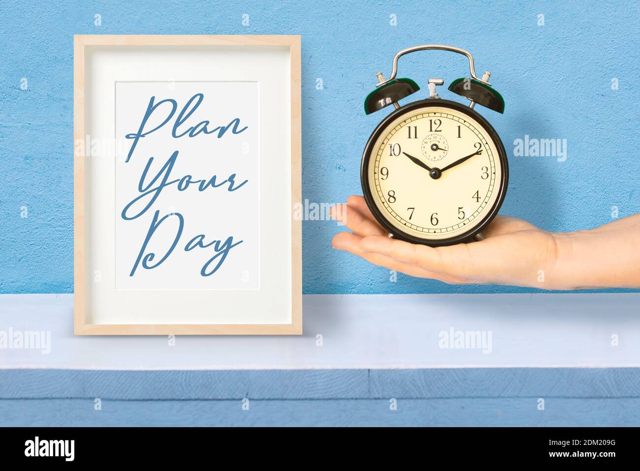 Hand holding an alarm clock next to a wooden frame with the sentence