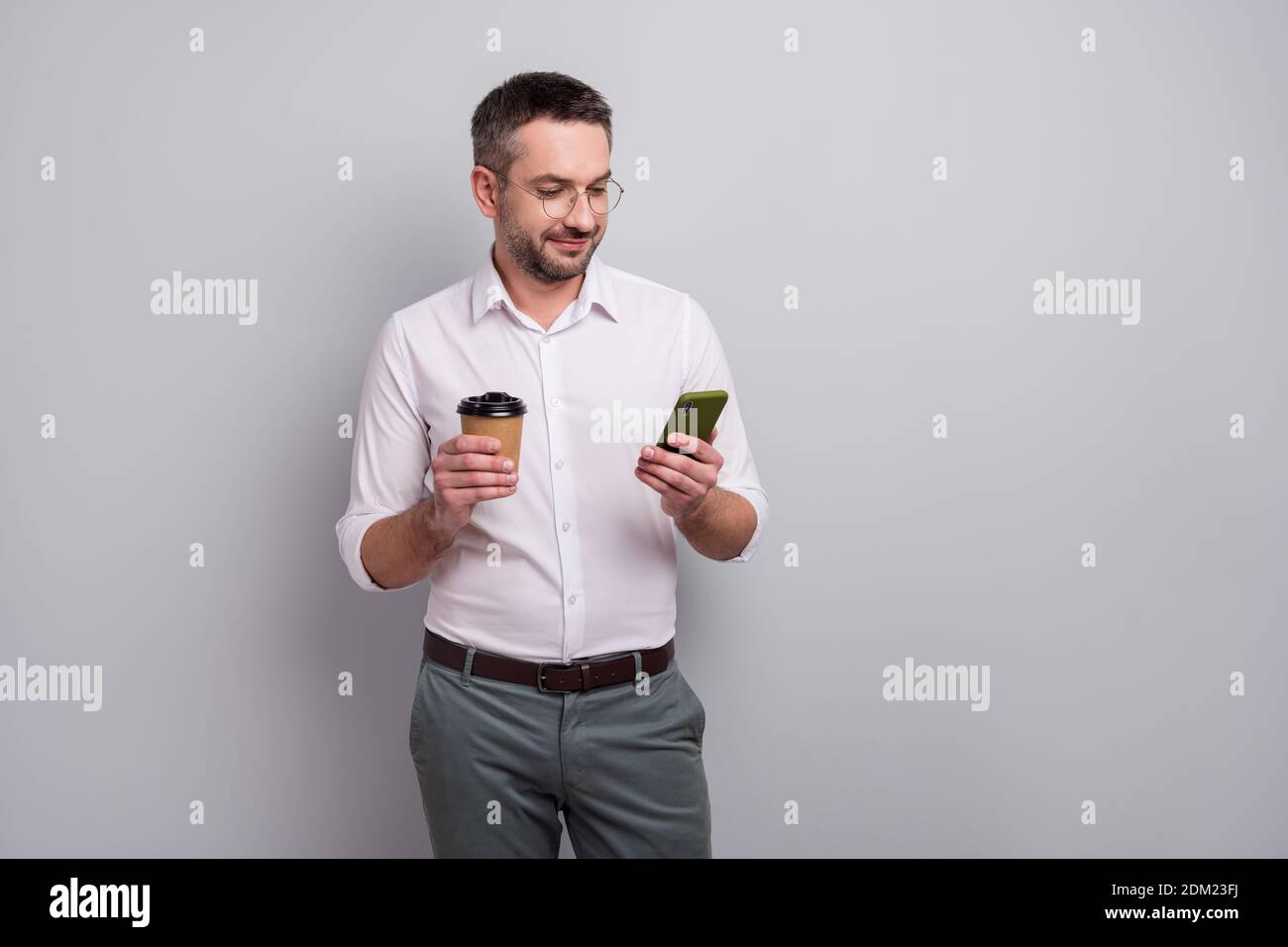 Portrait of his he nice attractive cheery elegant classy mature man holding in hands cell chatting online drinking cacao isolated over light gray Stock Photo