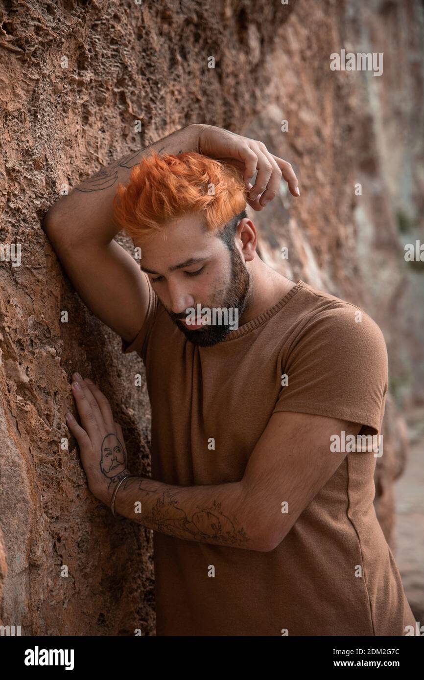 Portrait of young sad man with orange hair leaning on a stone wall Stock Photo