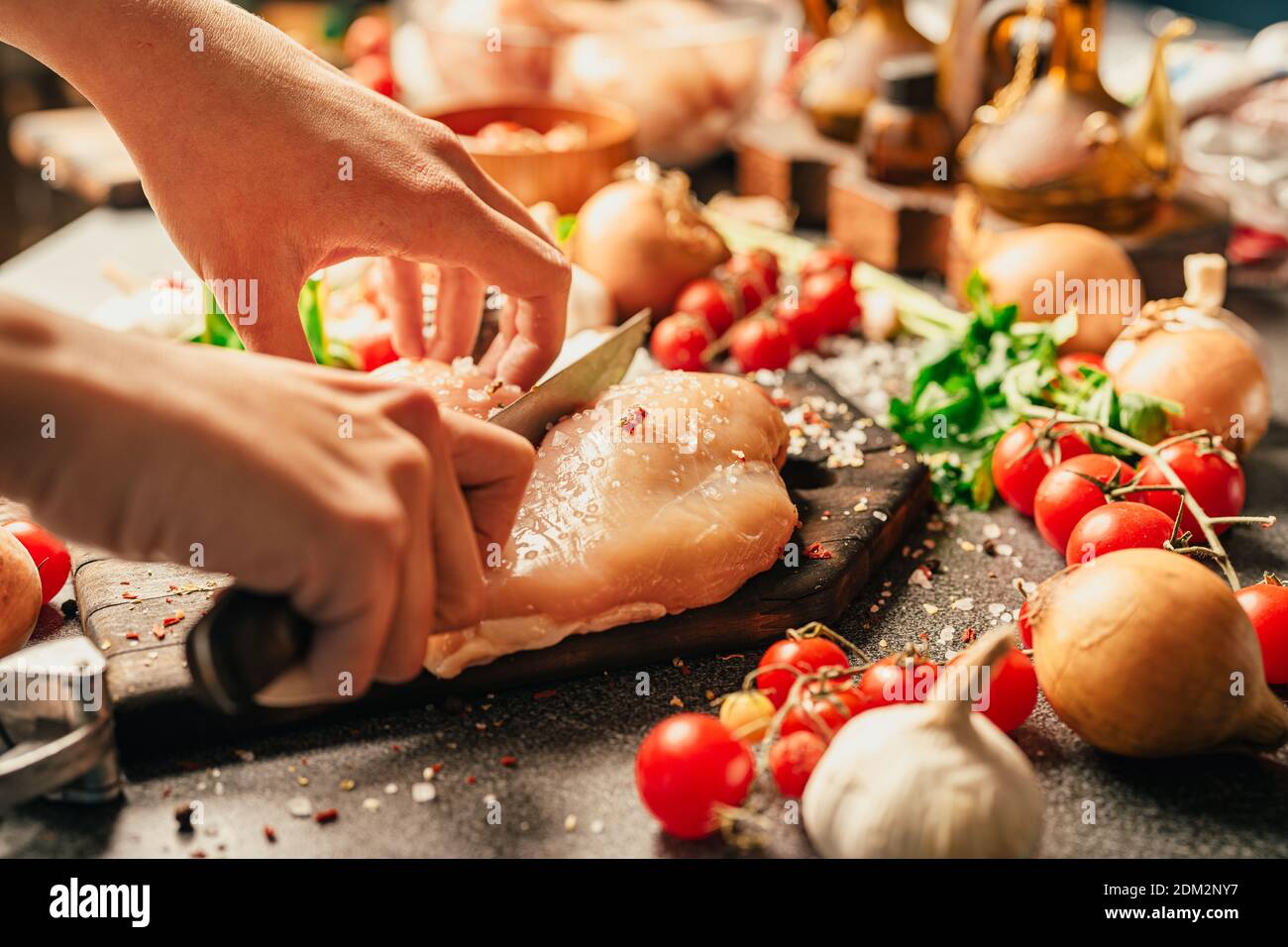 Housewife's hands cutting the fresh skinless boneless chicken breast with a knife on a wooden board.Seasoning and preparing raw chicken meat for lunch Stock Photo