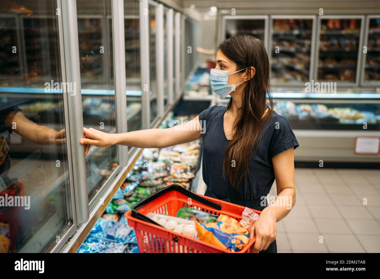 Young woman with protective face mask shopping for groceries in indoor groceries store.Coronavirus COVID-19 concept.Mandatory face mask in mall while Stock Photo