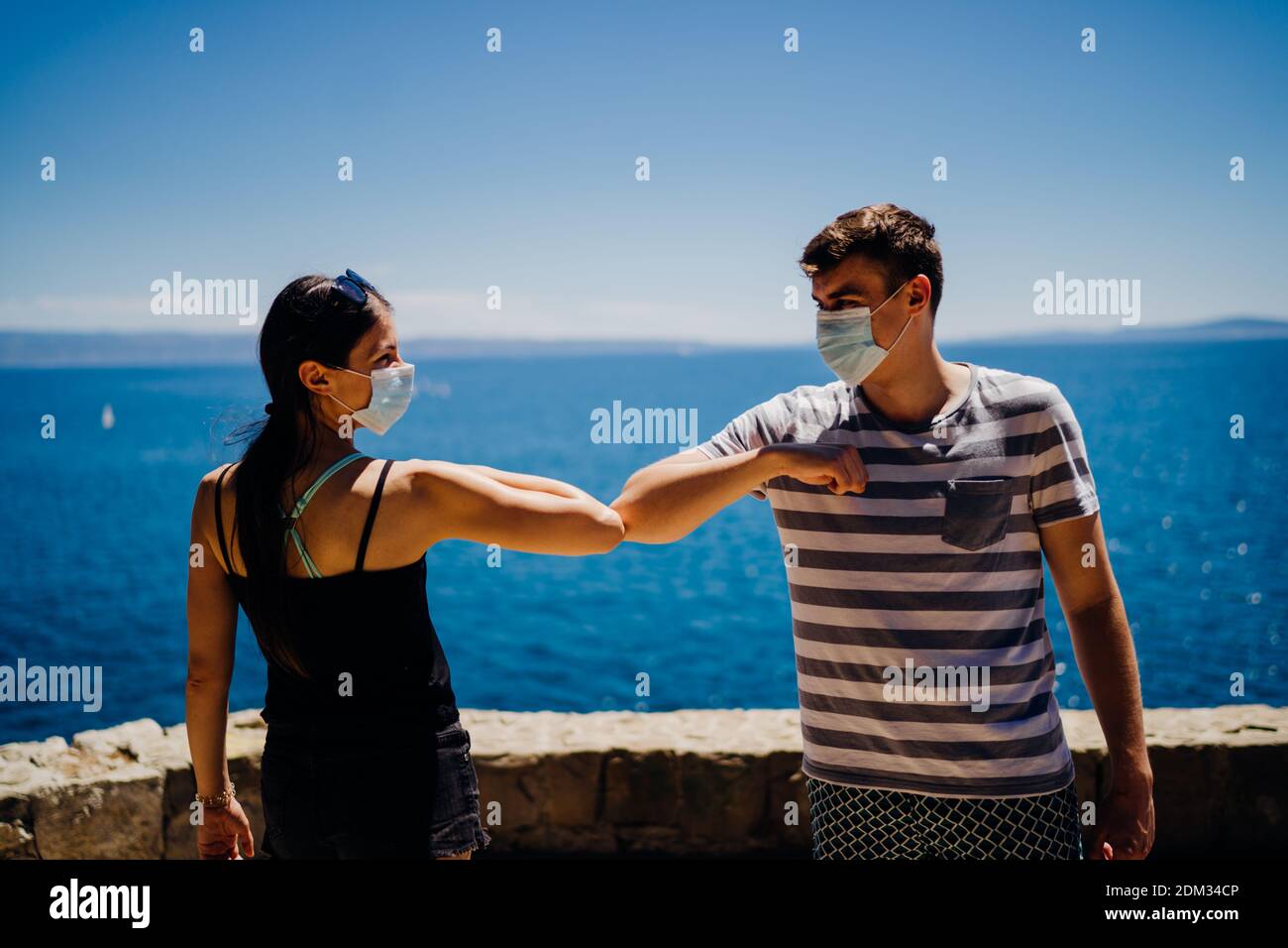 Two friends with protective masks greet with elbows bump. Alternative greeting during quarantine to avoid physical contact.Coronavirus COVID-19 disease Stock Photo