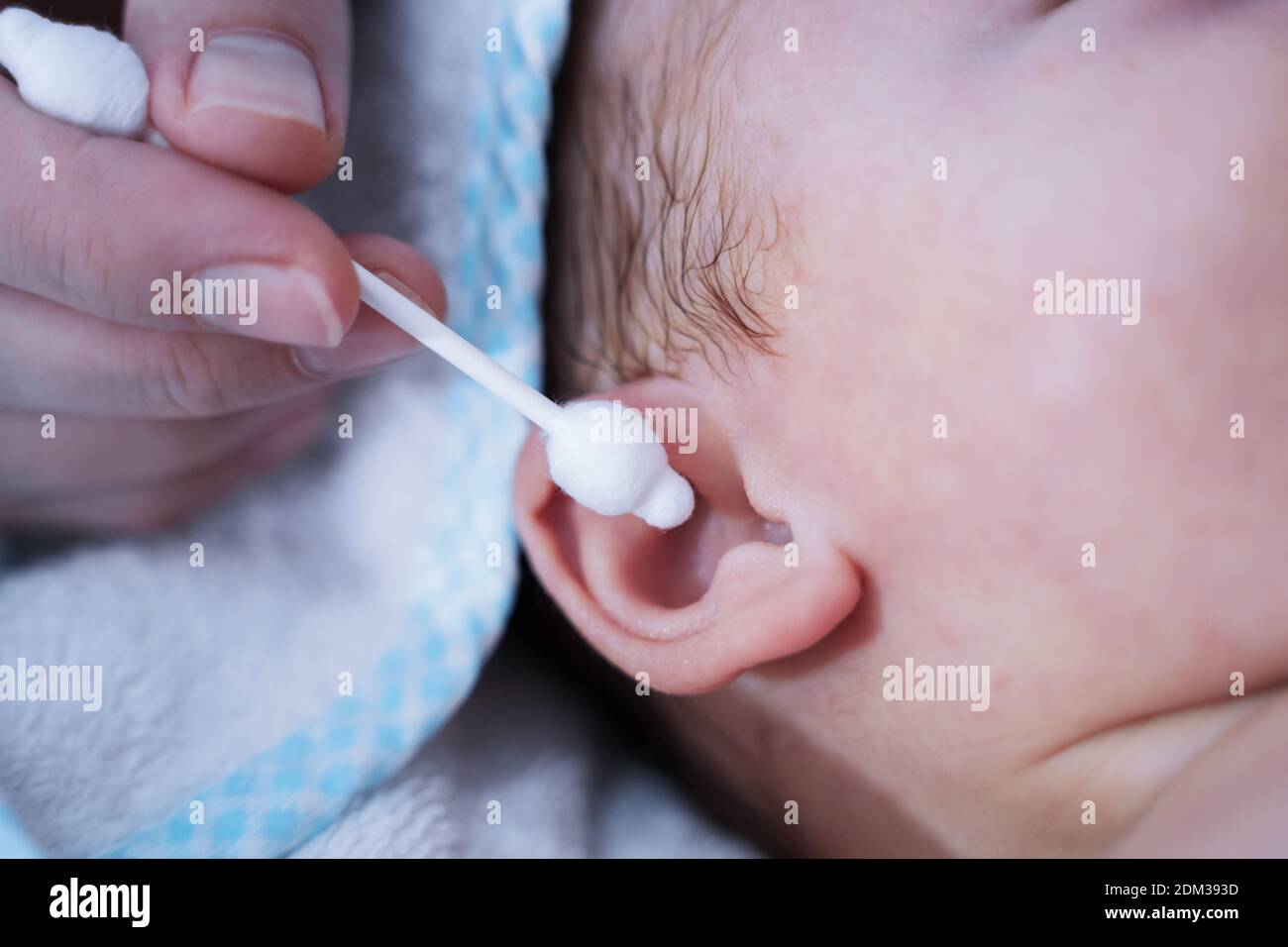 Mother cleaning newborn baby's ear with cotton swab. Newborn kid