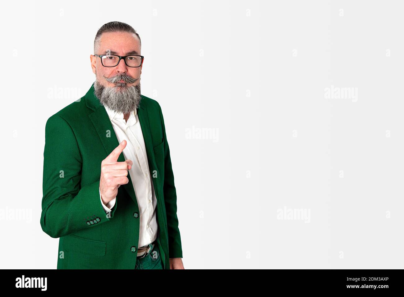 hipster in stylish green jacket and glasses standing isolated on white background, pointing with index finger and angry serious face frowning. Warning Stock Photo