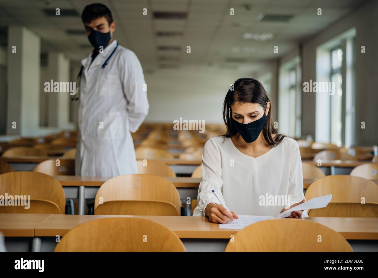 Female student taking an exam wearing a protective face mask in an empty amphitheater. Stressed student during COVID-19 outbreak.Coronavirus in-class Stock Photo