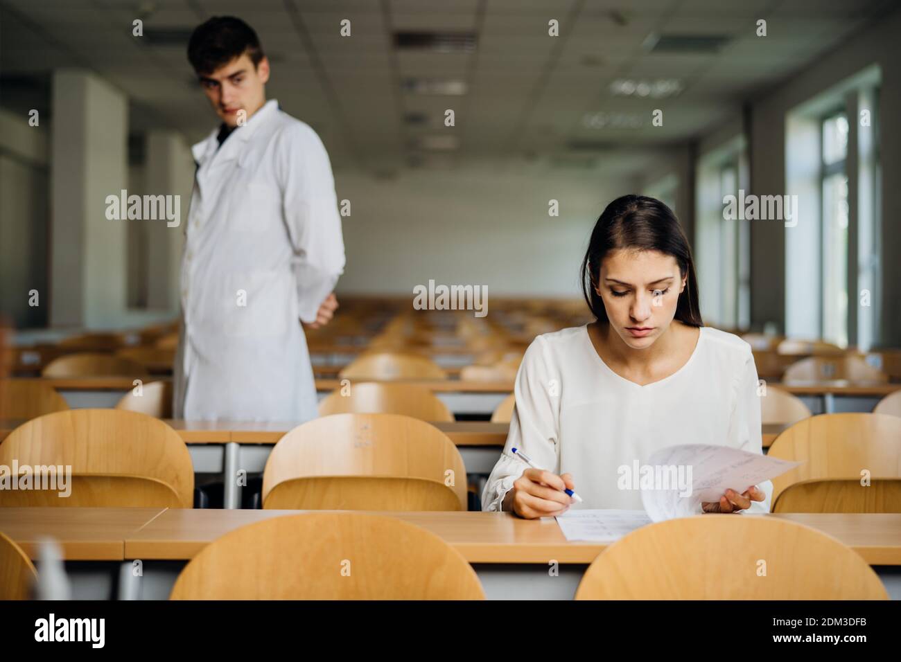 Female student taking an exam in an empty amphitheater. Stressed student taking in-class test. Concerned woman having education evaluation.Supervisor Stock Photo