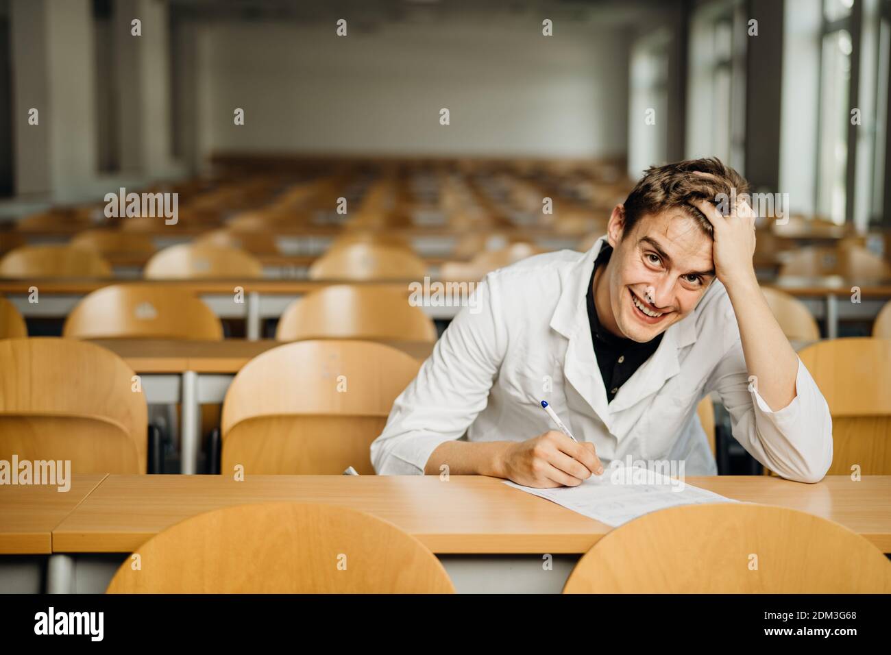 Knowledgable smiling student taking an easy exam in an empty amphitheater. An optimistic student taking an in-class test. Happy woman having stress fr Stock Photo