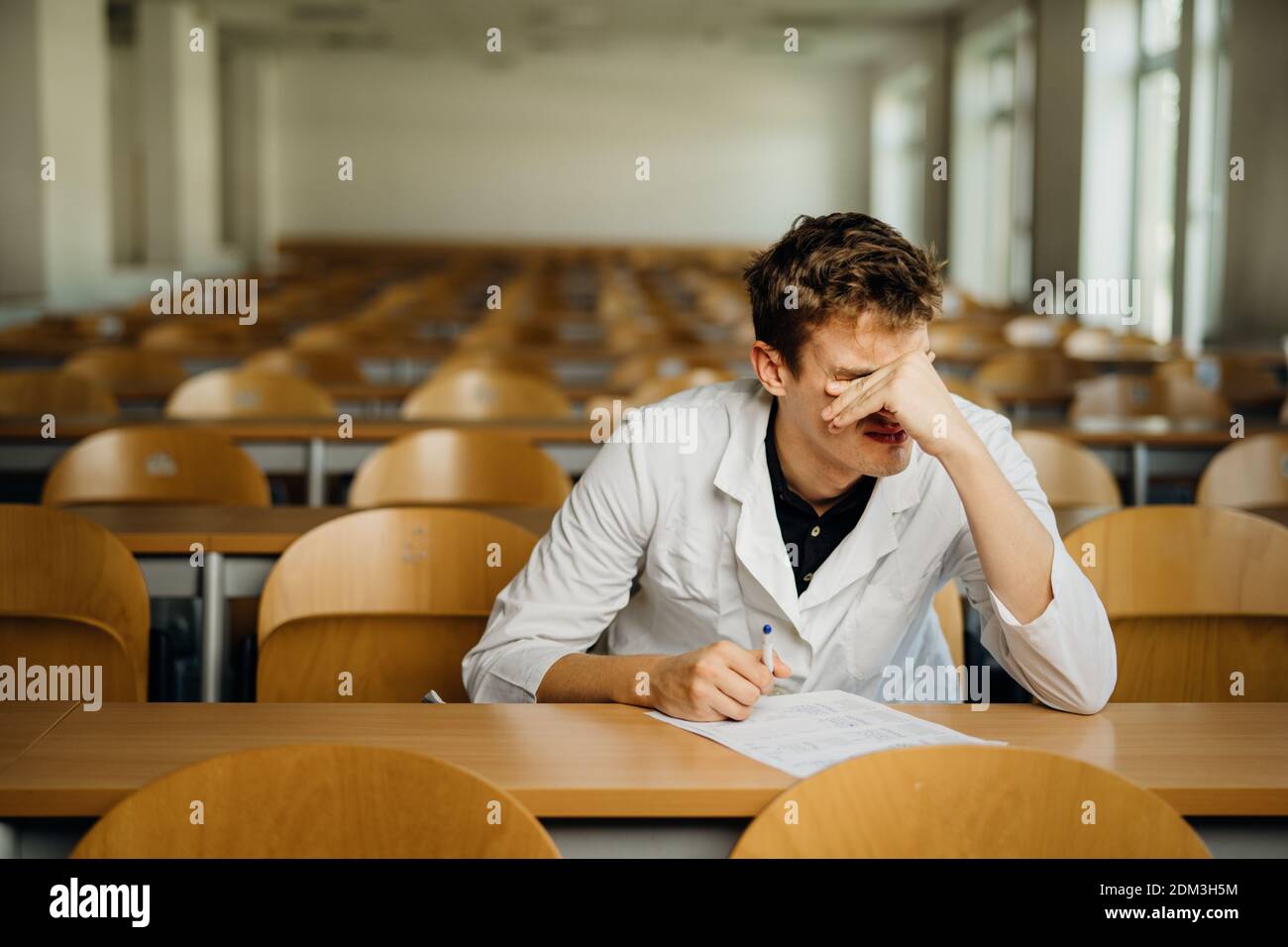 Medical professional filling out a document, looking exhausted, tired. Doctor writing an opinion.Medicine exam, medical practitioner taking test evalu Stock Photo