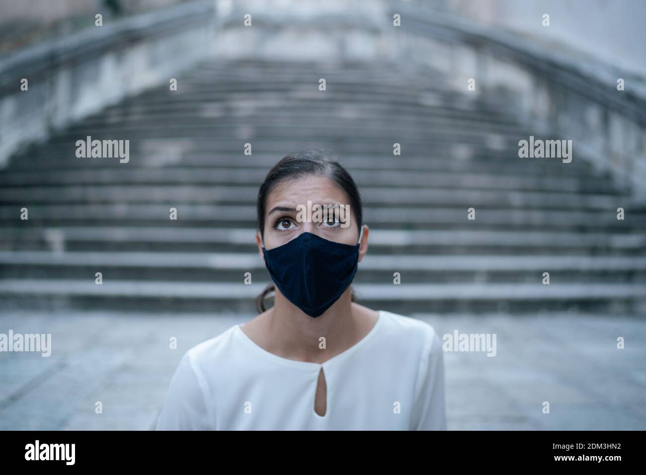 Fearful woman looking shocked/sceptic wearing a face mask in empty streets.Pandemic future concept.Negative emotions,stress,anxiety and panic amid cor Stock Photo
