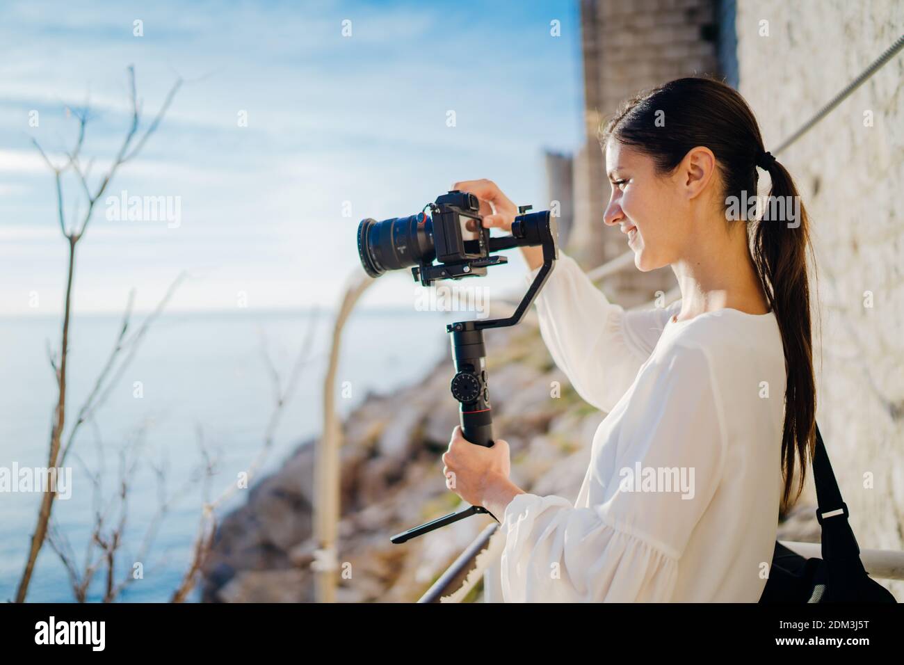 Smiling female travel vlogger video creator filming with a mirrorless camera on a gimbal stabilizer.Freelancer woman recording a low budget film for a Stock Photo