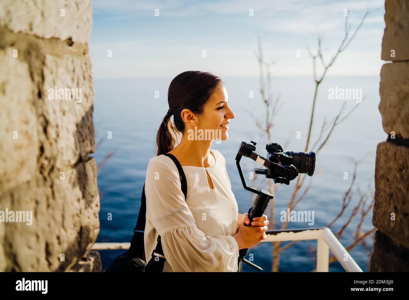 Smiling female travel vlogger video creator filming with a mirrorless camera on a gimbal stabilizer.Freelancer woman recording a low budget film for a Stock Photo