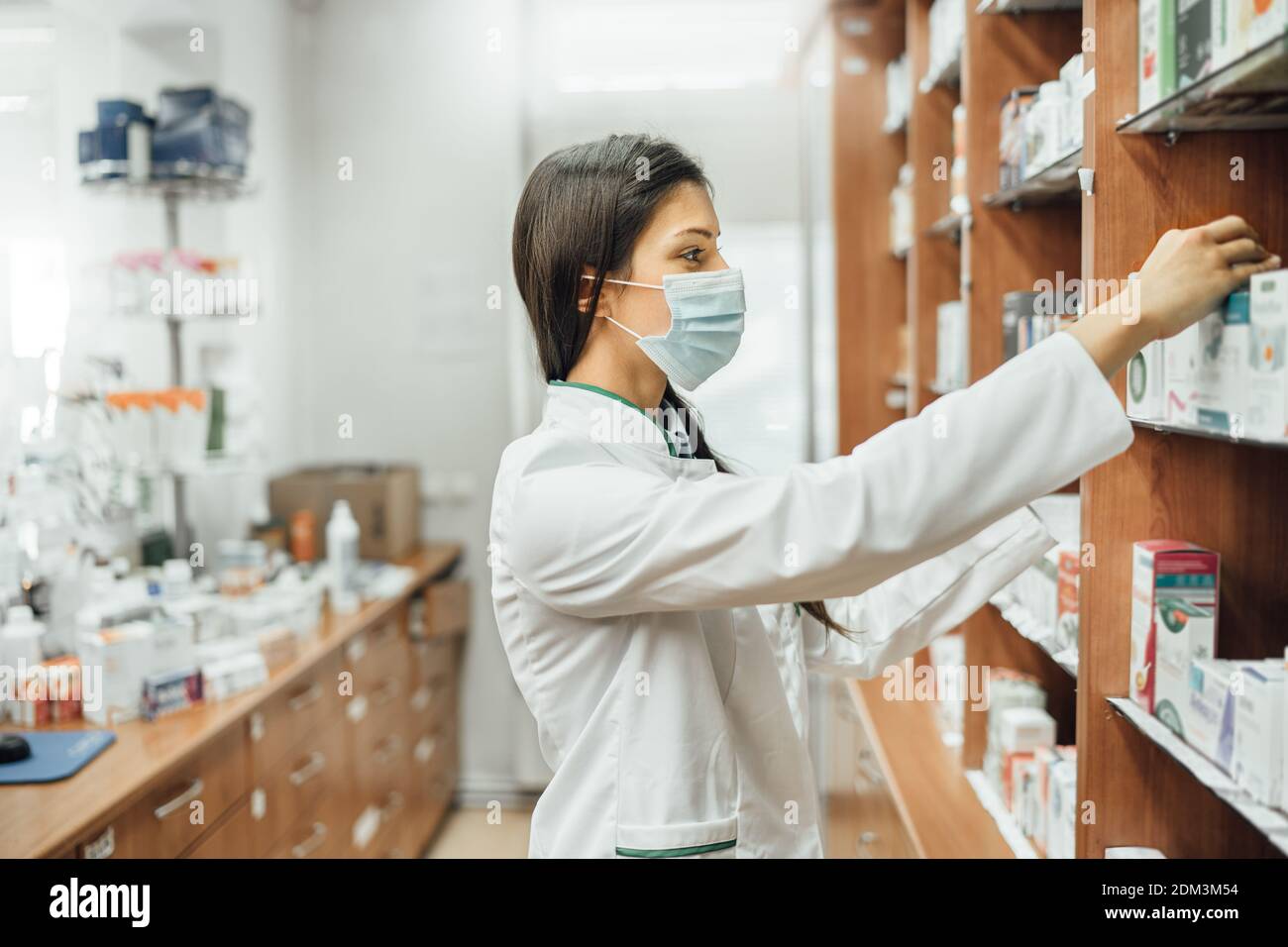 Pharmaceutical professional working in a pharmacy during COVID-19 outbreak.Young pharmacist wearing a protective mask.Coronavirus pandemic health care Stock Photo