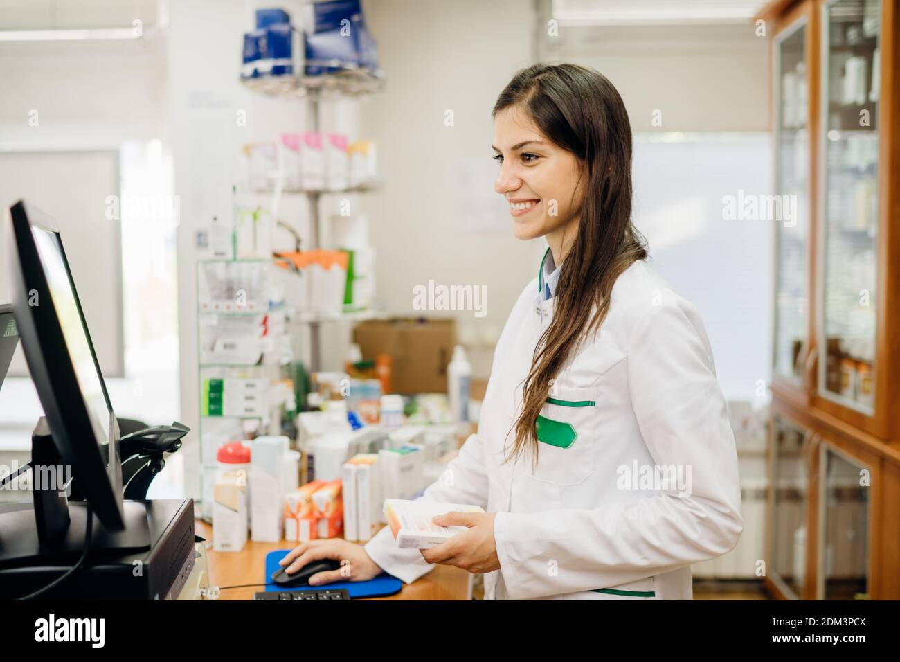 Smiling friendly pharmacist at the counter working in a pharmacy store. Pharmaceutical professional recommending an over the counter supplement. Remot Stock Photo