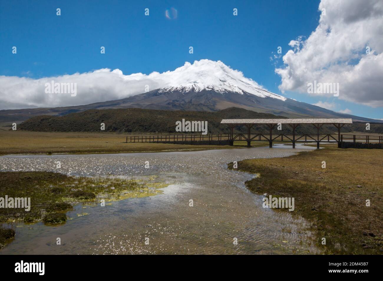 The snowcapped Cotopaxi Volcano with a lake  (Laguna Limpiopungo) and footbridge in foreground. Cotopaxi National Park in the Ecuadorian Andes. Stock Photo