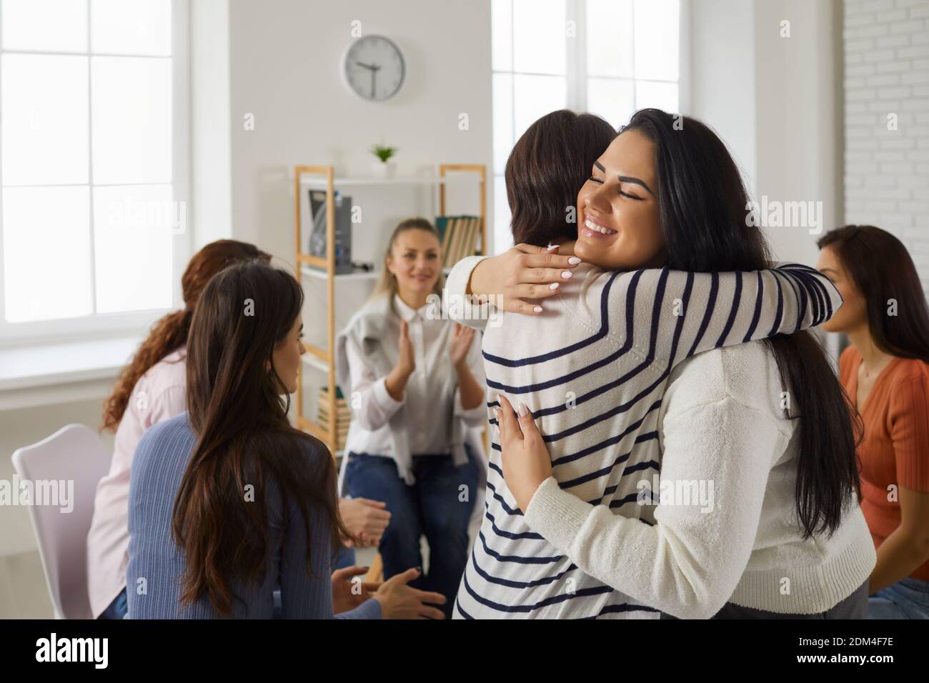 Happy young women hugging each other in support group meeting or therapy session Stock Photo