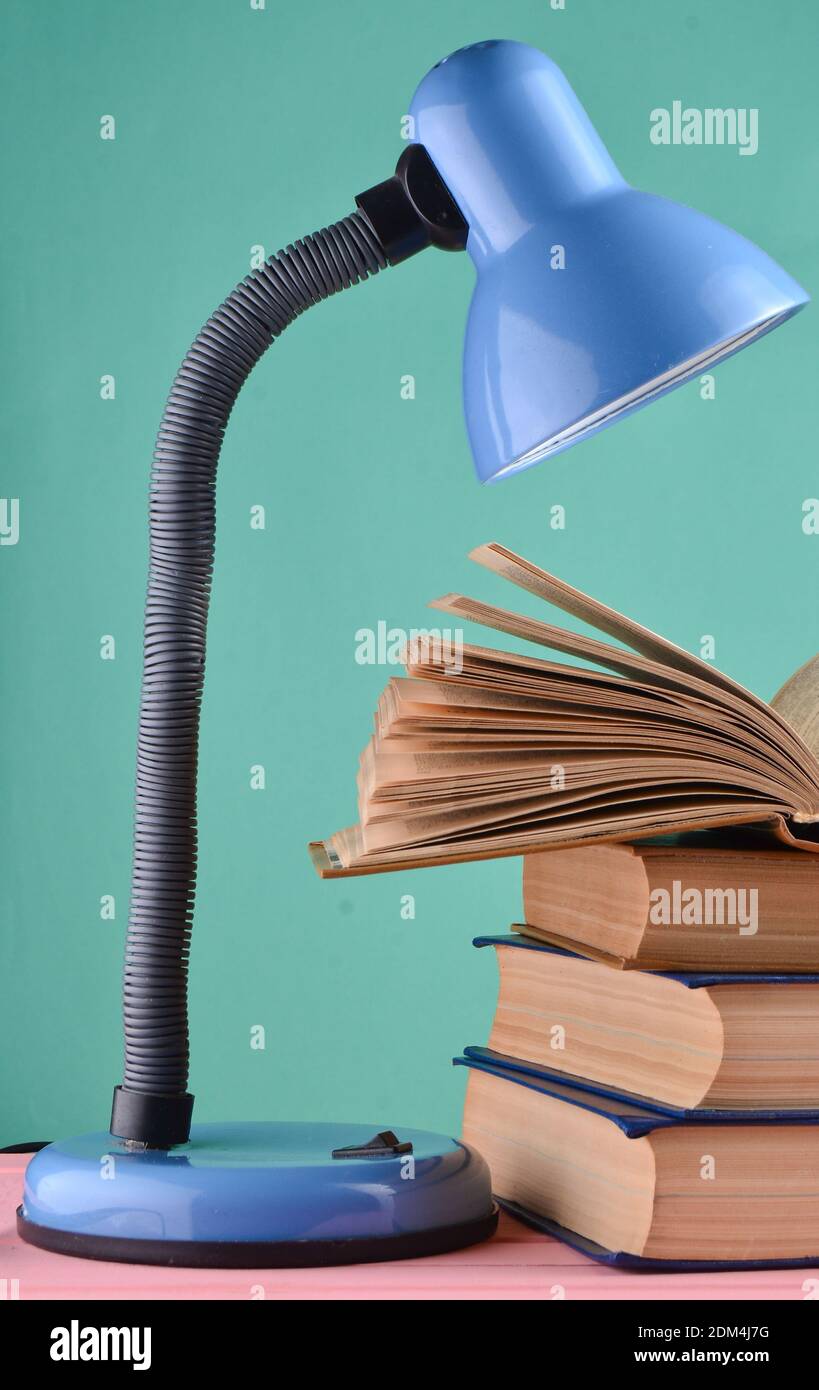 A table lamp and a stack of books on a table isolated against a blue ...
