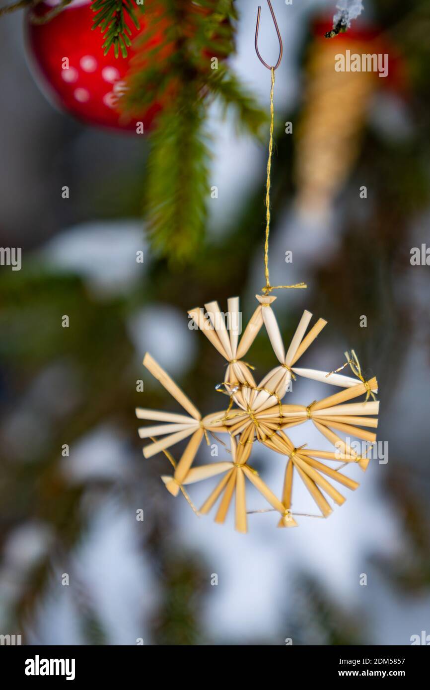 Weihnachtsdekoration Outdoor, Strohstern und Christbaumkugel im Tannenwald mit Schnee im Hintergrund. Christmas Tree Decoration in Corona Time Stock Photo