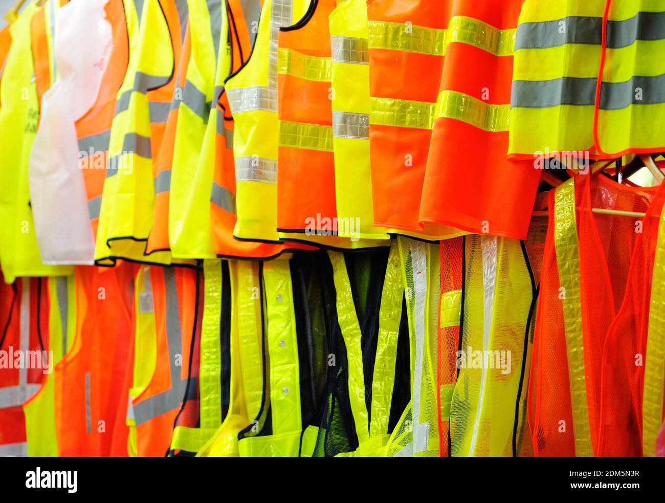 Collection of security reflective cloths, orange and yellow, hanging in row vests. Stock Photo