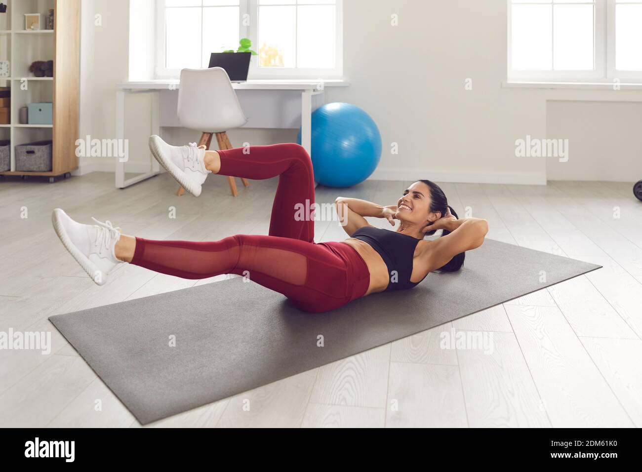 Cheerful sporty young female lying on gym mat at home and doing bicycle crunches Stock Photo