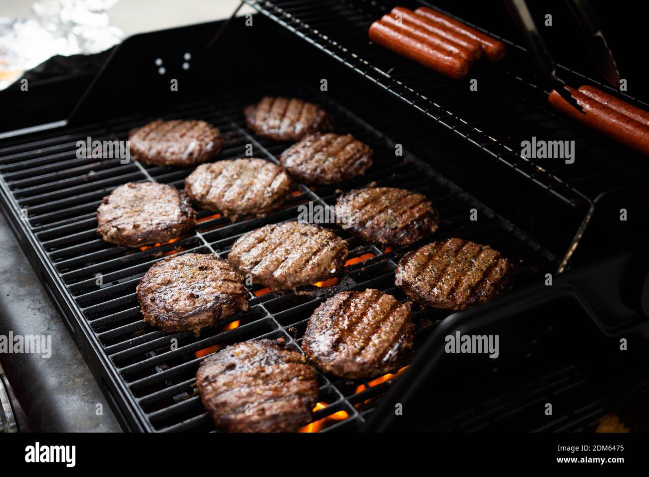 Hamburgers and hot dogs cook on flame charred backyard grill Stock