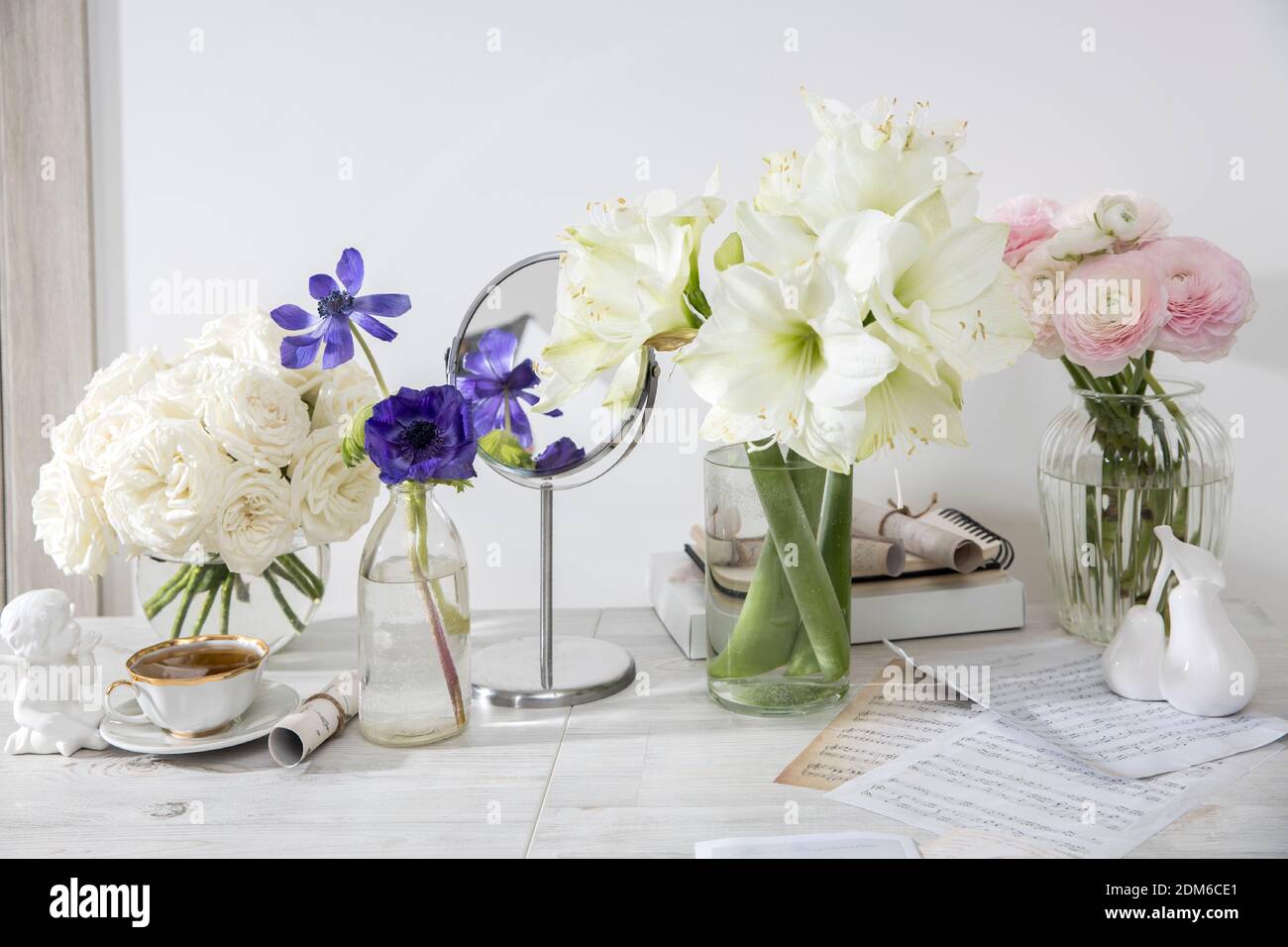 A bouquet of white roses in a round glass vase, a bouquet of white amaryllis, a cup of tea, a figurine on the table. Decoration of the kitchen. Rose P Stock Photo