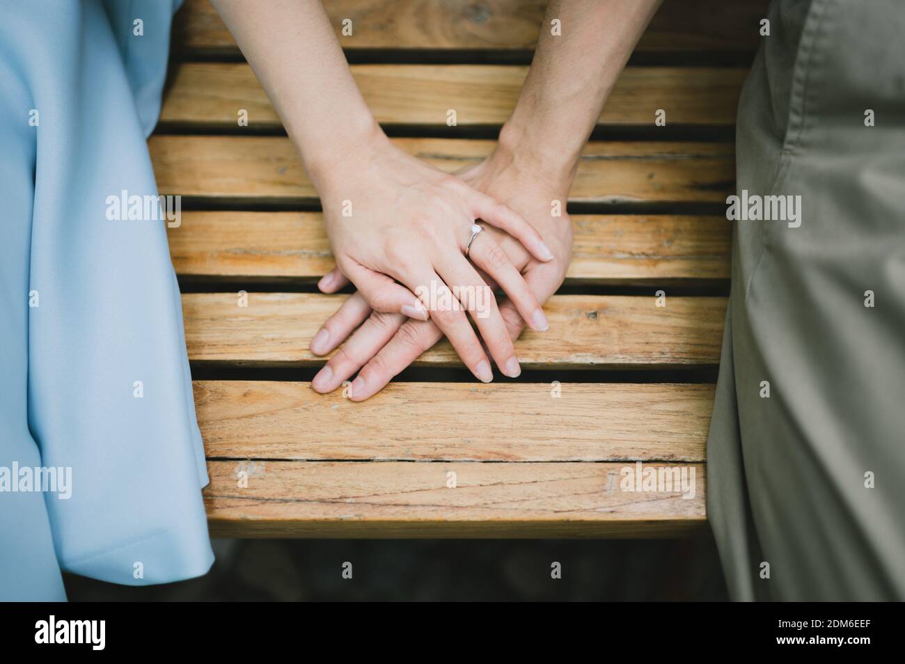 Midsection Of Couple Holding Hands While Sitting On Bench Stock Photo