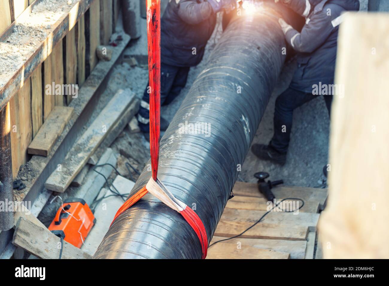 Professional welder welding water or gas steel pipeline in protective trench and mask at