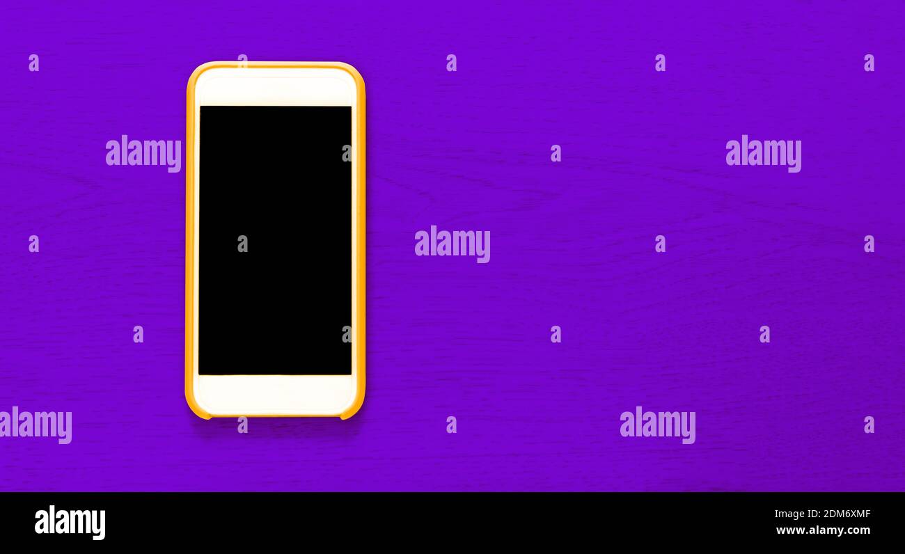 Top view of yellow cell phone with isolated black screen that contrasts with purple background with wood texture and ample copytext space. Smartphone Stock Photo