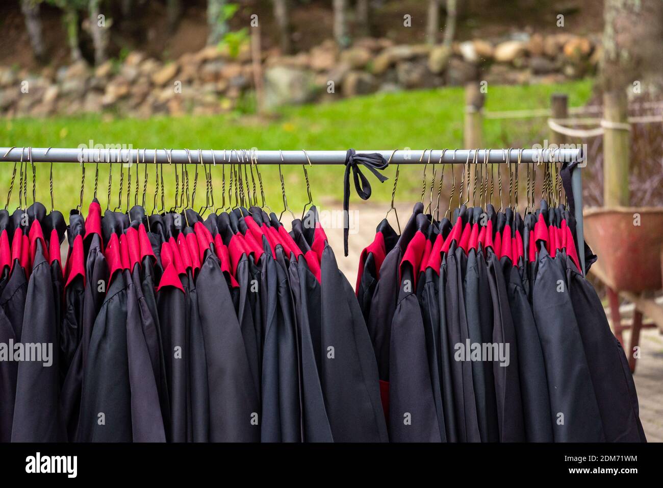 Black and Red Graduation Gowns Hanging From a Metal Tube in a Garden