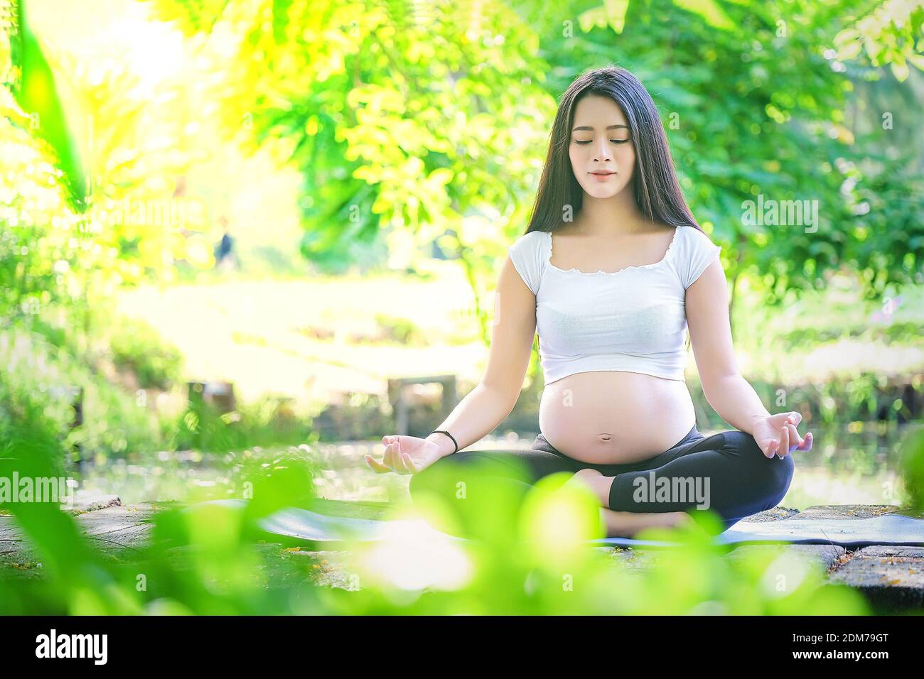 Pregnant Woman Mediating While Sitting On Footpath Against Trees In