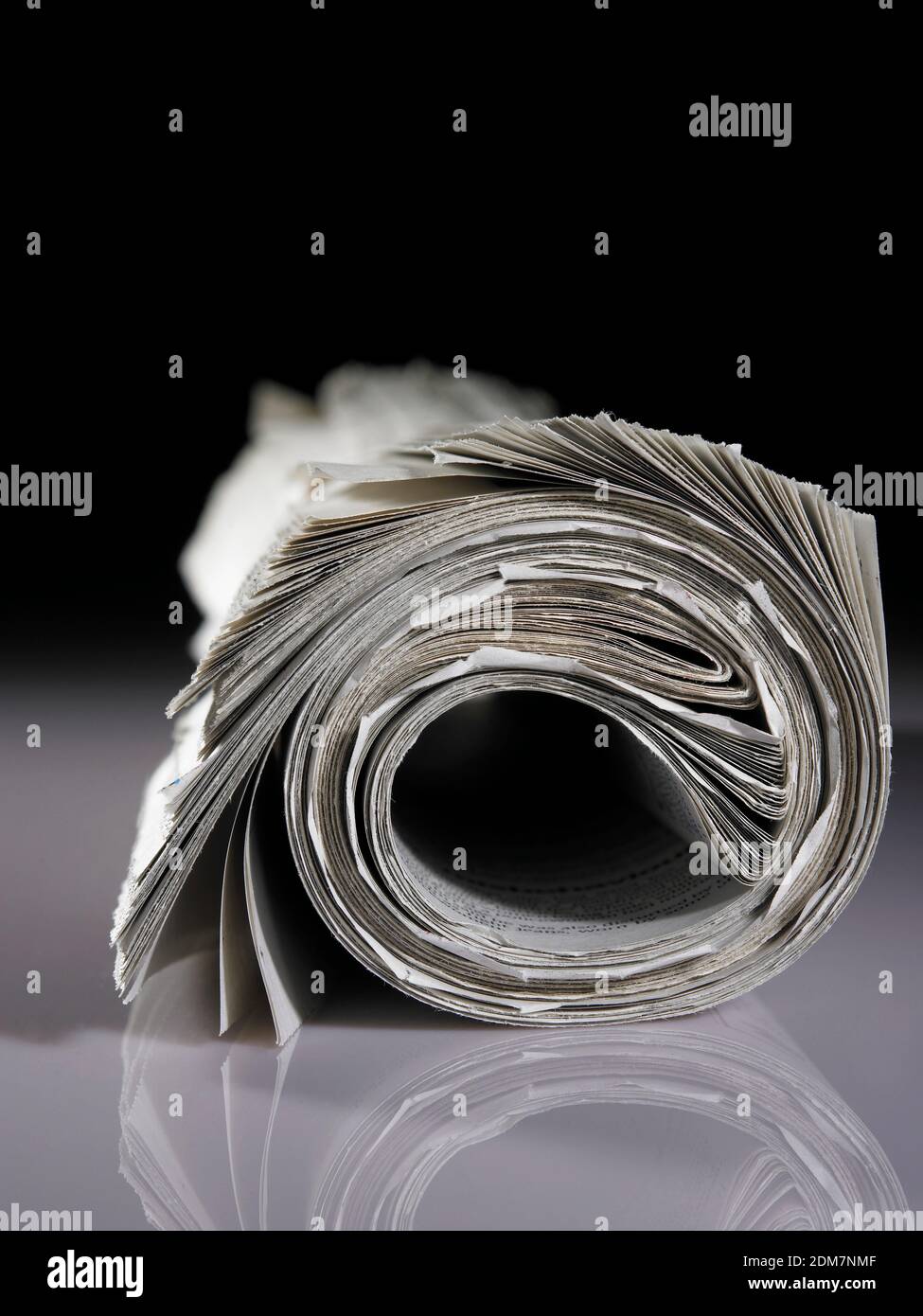 Closeup Of Newspaper Rolled Up On Table Against Black Background Stock