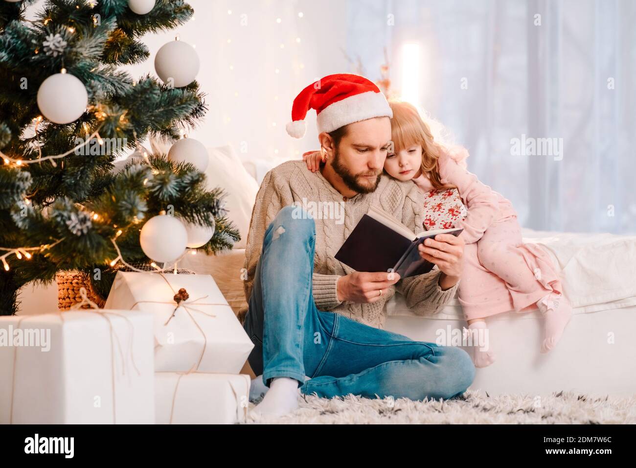 Dad in santa hat reading book with his daughter. Father reading fairy tale to a child Stock Photo