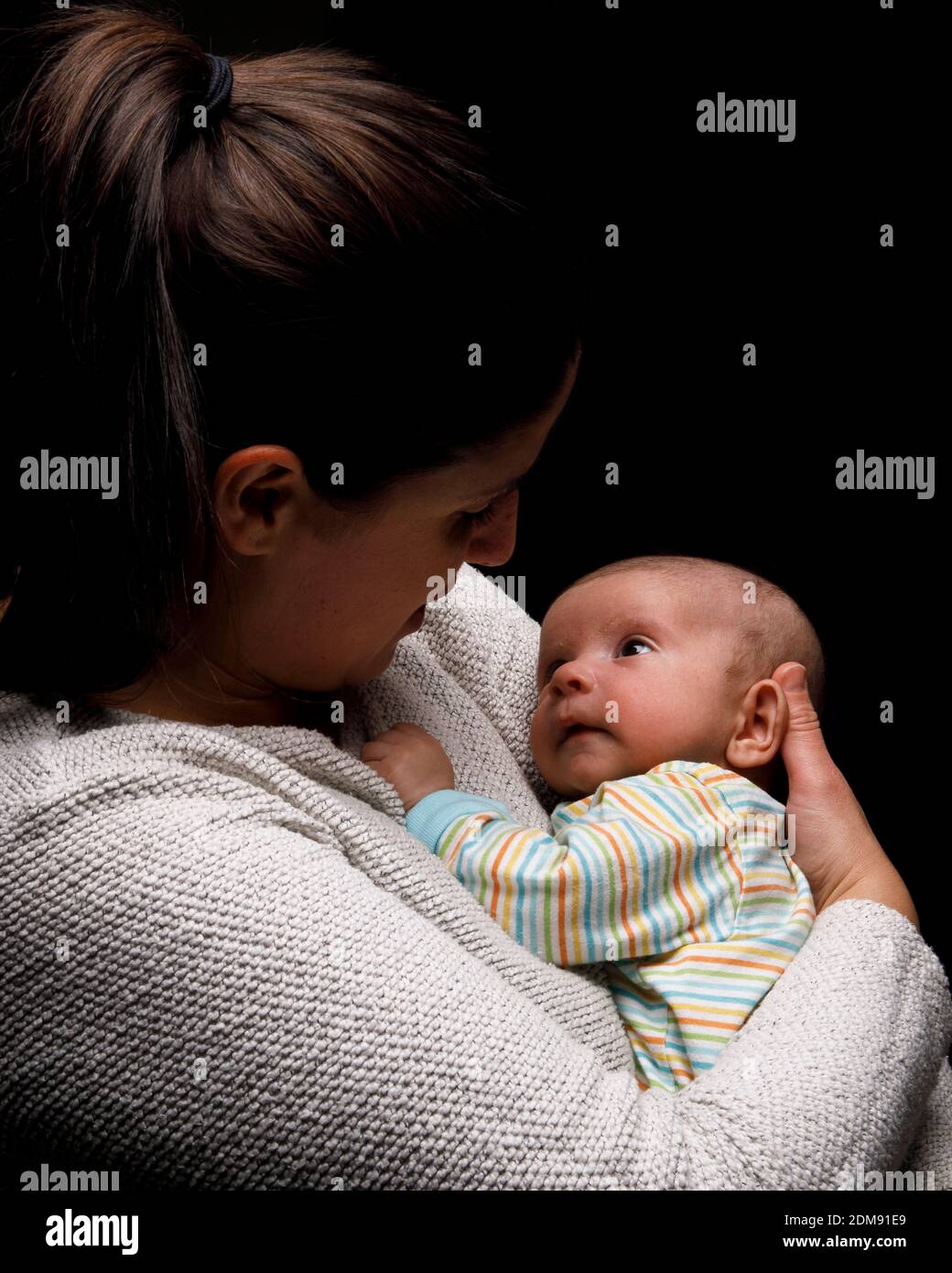 Side view of happy mom cuddling adorable newborn baby and enjoying moments of motherhood against black background Stock Photo