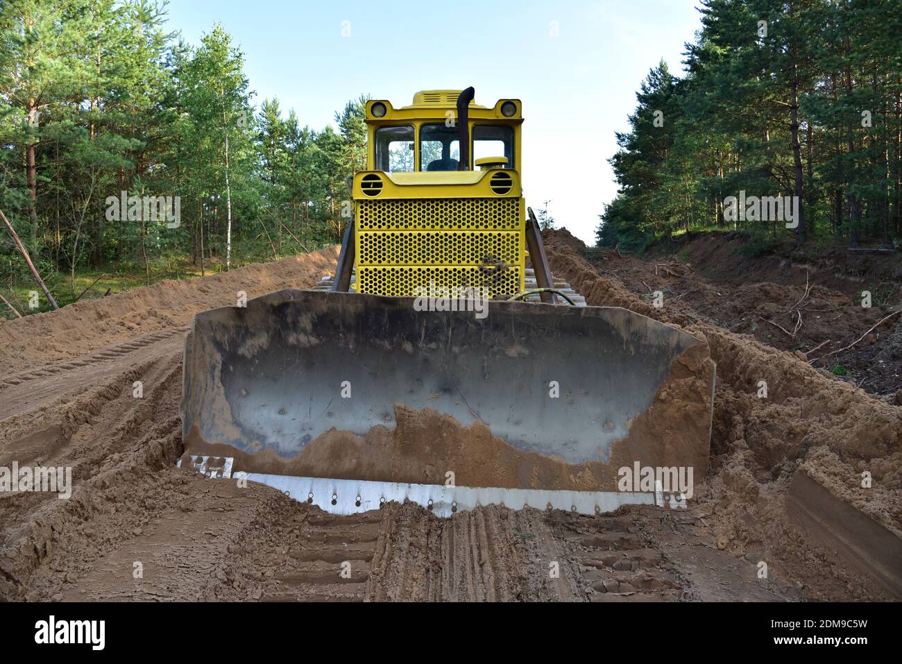 Dozer during clearing forest for construction new road . Yellow Bulldozer at forestry work Earth-moving equipment at road work, land clearing, grading Stock Photo