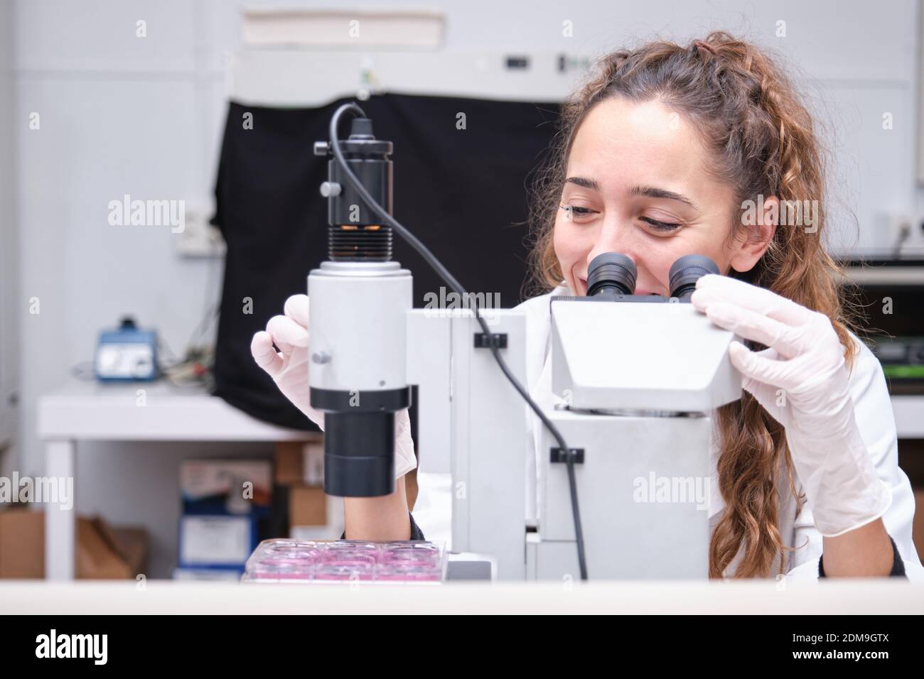 Young female scientist looking through a microscope in a laboratory. Laboratory research concept. Stock Photo