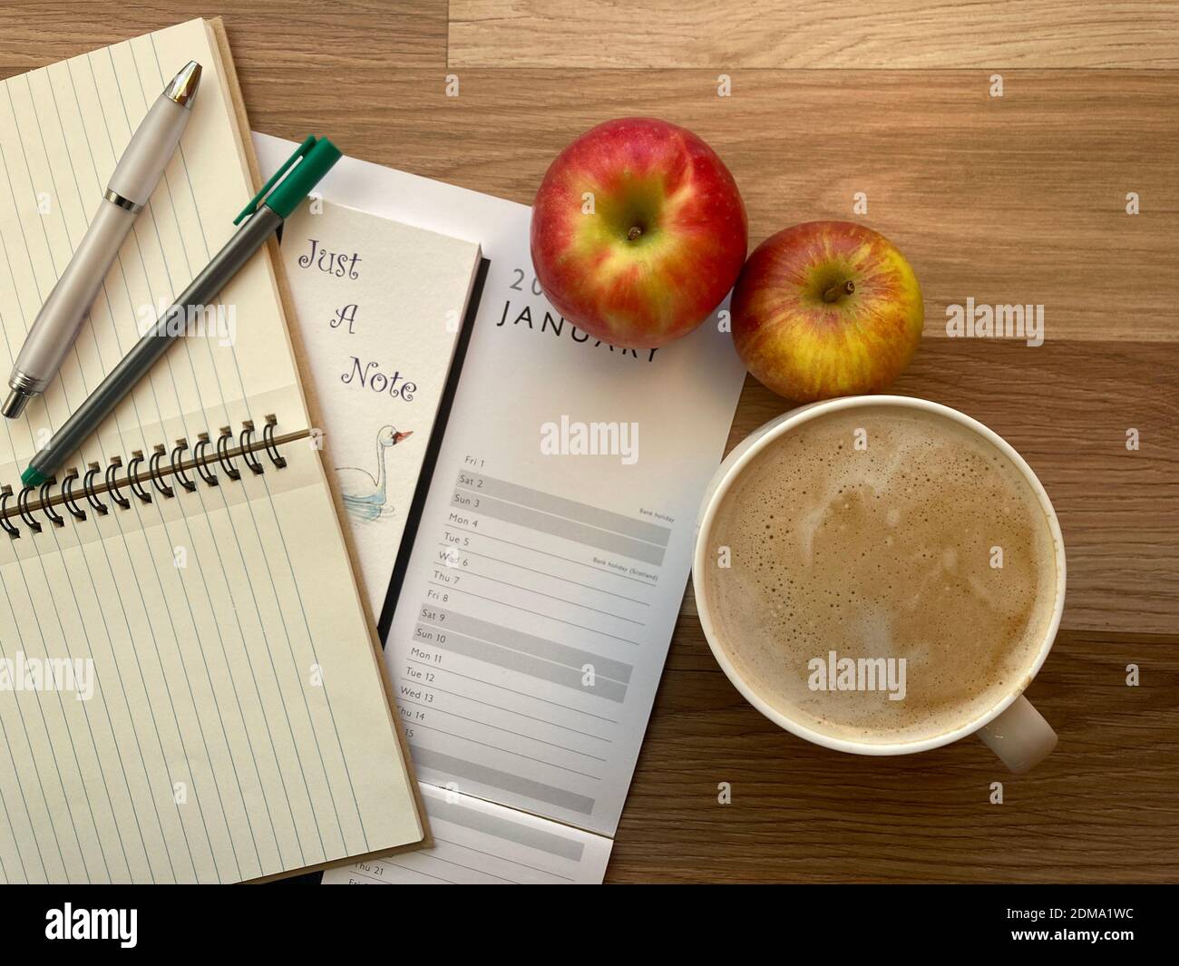 Calendar on desktop, with notebooks, pens, coffee and apples Stock Photo