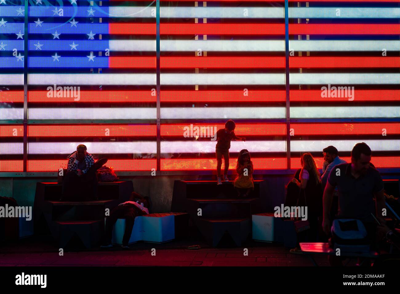 NEW YORK, UNITED STATES - Nov 18, 2020: Visitors to Times Square are silhouetted against an American flag in Manhattan, New York City. Stock Photo
