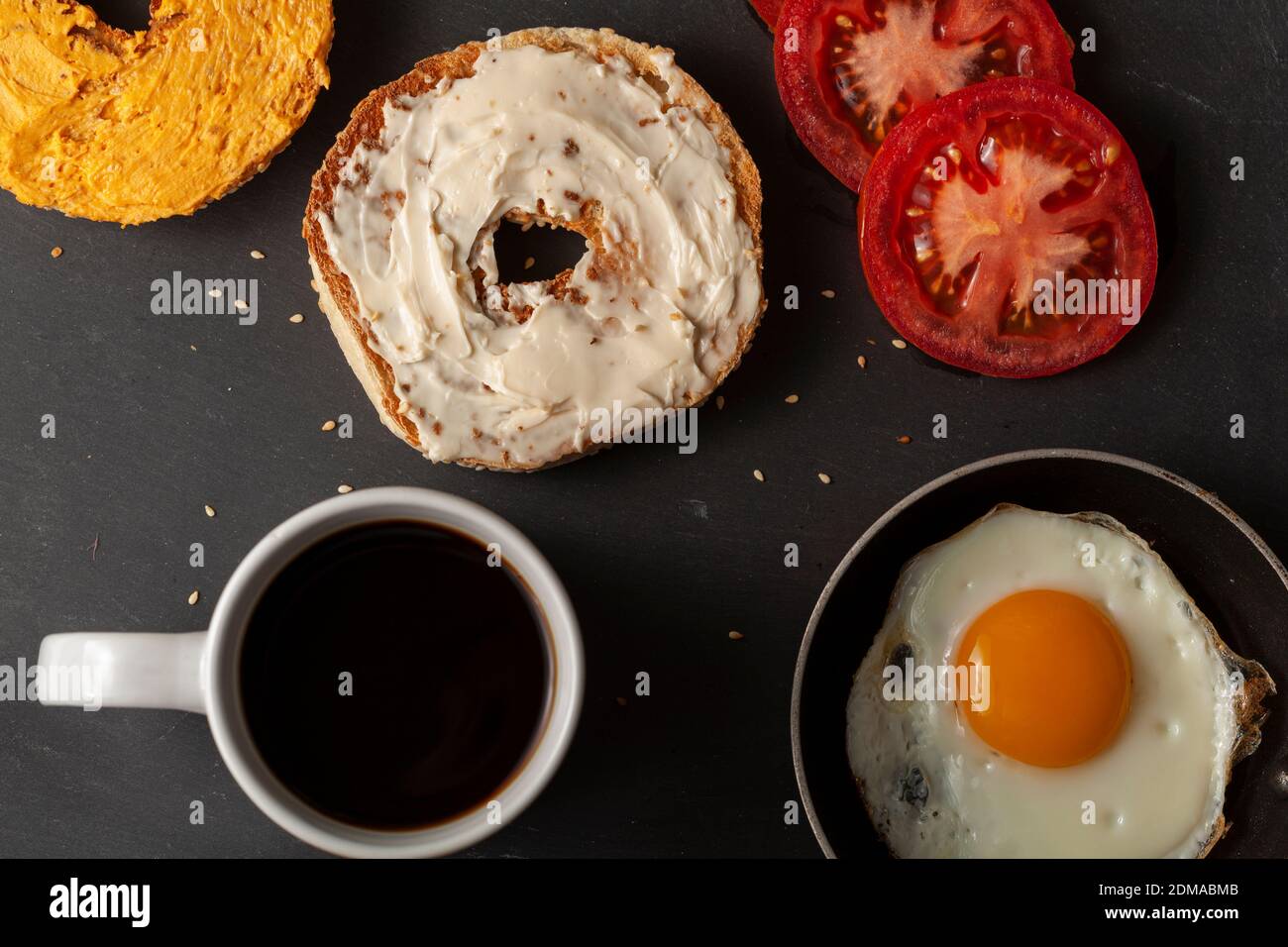 A flat lay breakfast or snack  for one person featuring a sesame bagel toasted and sliced in half with pub cheese and cream  on, slices of tomato, sun Stock Photo