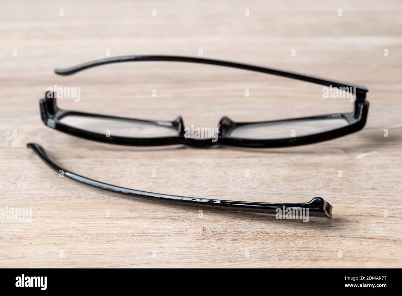 One eyeglasses temple in front of broken spectacles on a brown desk