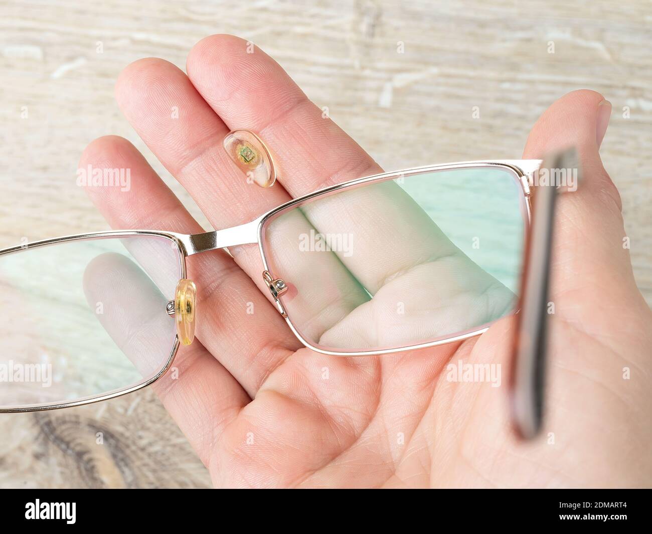 Eyeglasses and nose pad broke off them on a hand palm against brown desk. Spectacles with