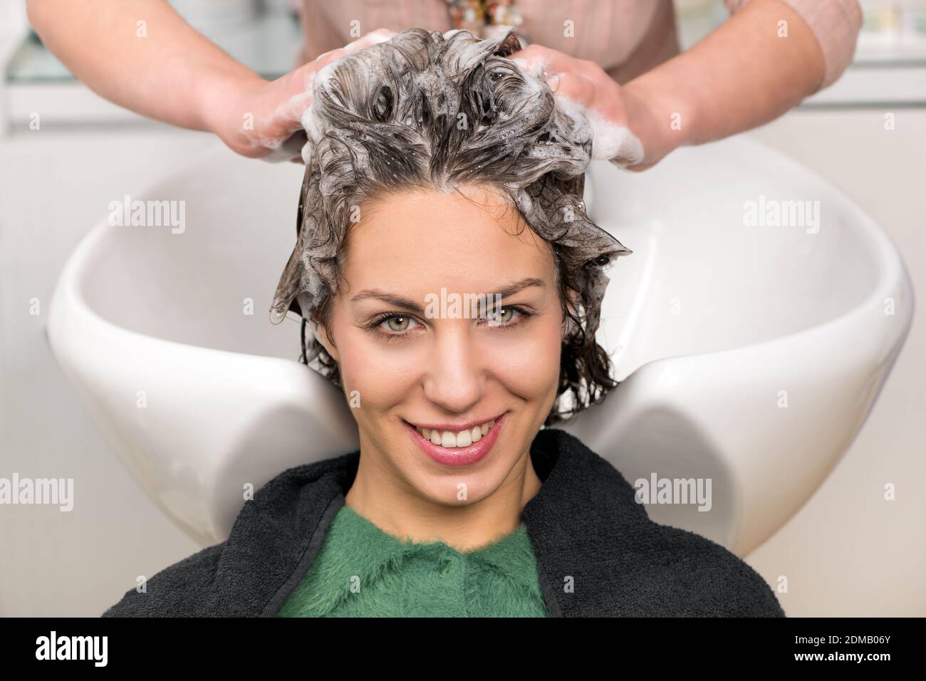 Cute young girl having her hair washed with shampoo by the hands of  professional hairdresser at