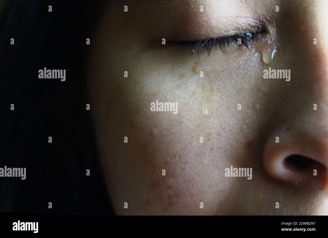 Closeup half face of Asian woman crying with tears, isolated on dark