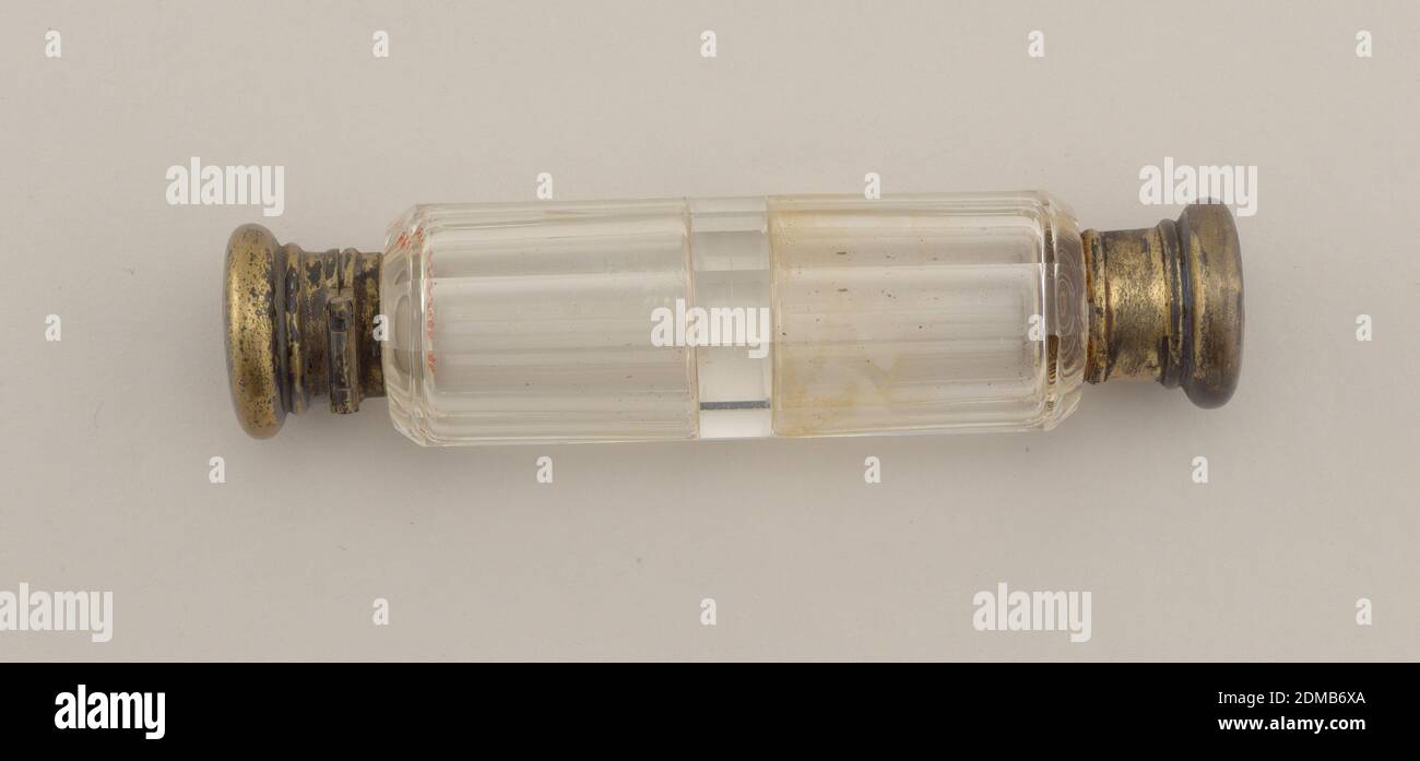 Bottle, Glass, gold plate, metal, Iin shape, a polygonal cylinder, bevelled at each end, with flat shoulders leading to necks. Ends fitted with gold-plated collars with pancake-shaped covers of larger diameter than collars but less than body of the bottle. One cover hinged. Glass divider across center of cylinder is a thick wall of glass. Monogrammed on end, 'E. A. T.' in interlaced letters., USA, late 19th century, glasswares, Decorative Arts, Bottle Stock Photo