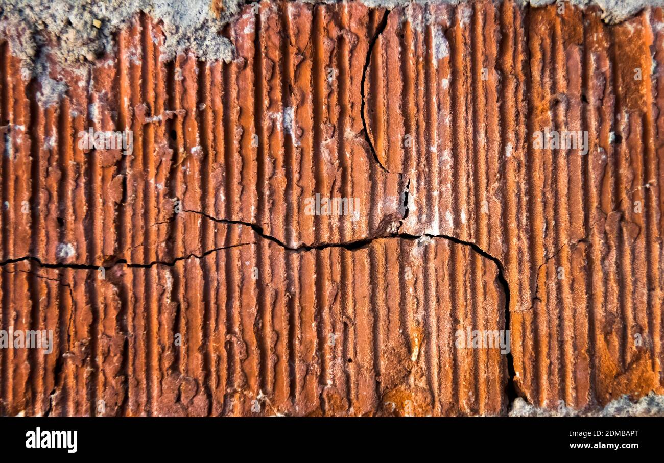 Old cracked brick in close up detail with deep red texture and a crack running throughout. Stock Photo