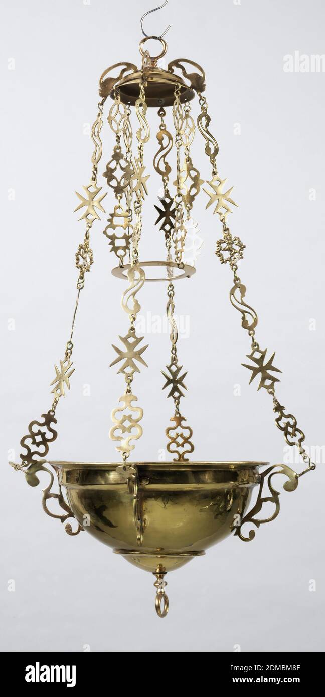 Altar lamp, Brass, Prefericulum shaped, and suspended by four chains from an inverted bowl. The chains return, and support a round ring which hangs, centered to the main body of the lamp and about ten inches above it. The main body of the lamp is unadorned save for two fillets, a rolled, splayed rim and a ring which is attached to the lowermost point of the lamp. The inverted bowl is decorated by a torus and surmounted by a ring. Four handles in wrought scroll shapes act as brackets for the four suspension chains. The links of the chains are wrought in forms of bucklers, Maltese crosses Stock Photo