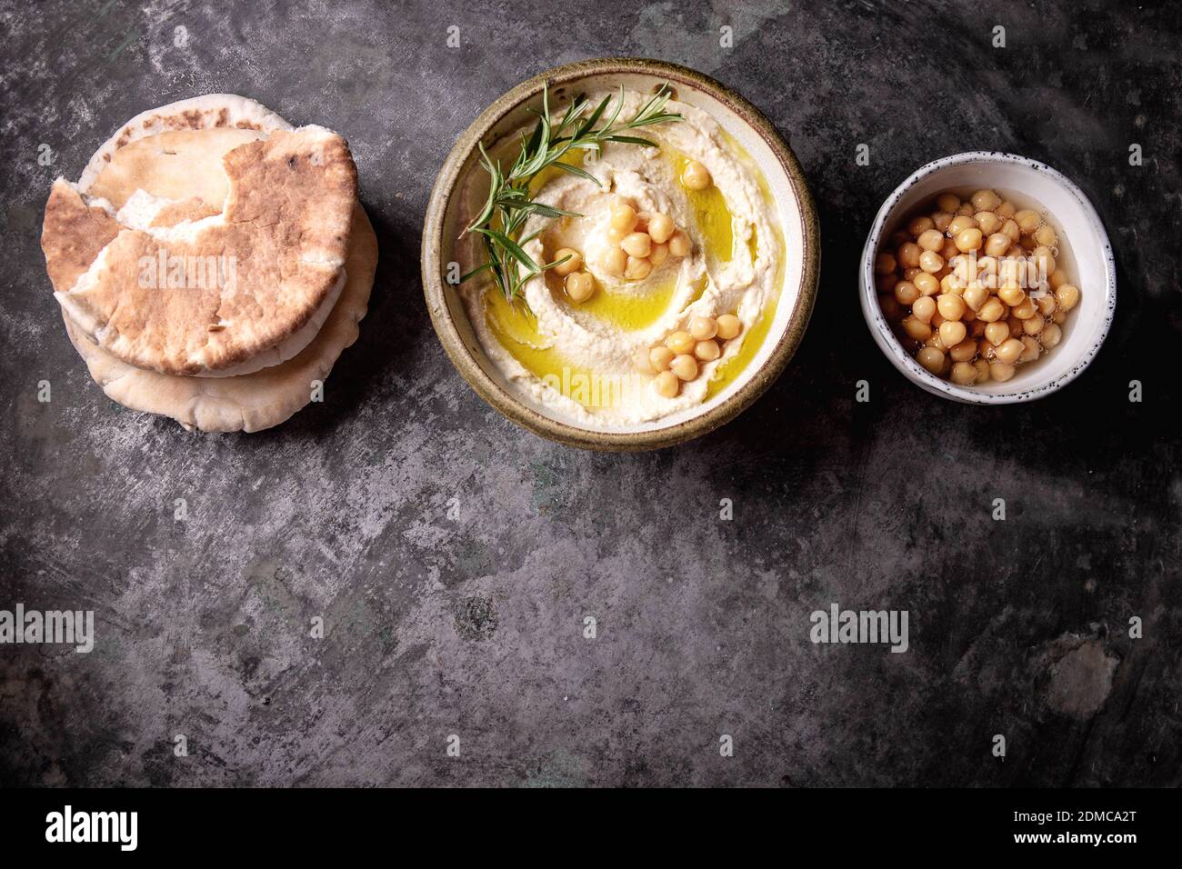 Home made hummus bowl, decorated with boiled chickpeas, herbs, pita and olive oil over a rustic metal background. Top View. Stock Photo