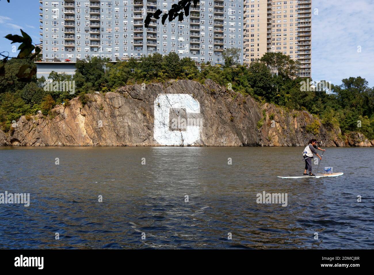A stand-up paddler paddles by the Big C Rock on the banks of Spuyten Duyvil in New York, NY. Stock Photo
