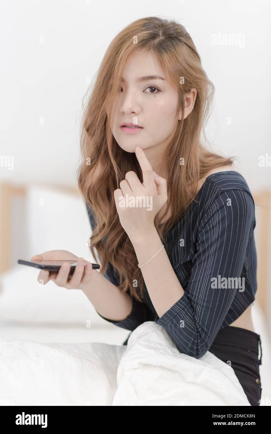 Portrait Of Beautiful Young Woman Using Mobile Phone While Sitting On Bed At Home Stock Photo