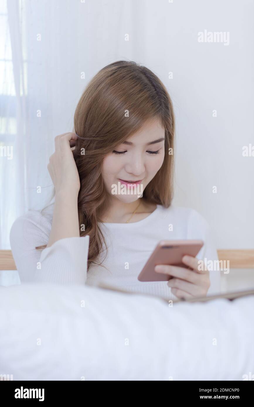 Young Woman Using Mobile Phone While Sitting On Bed At Home Stock Photo